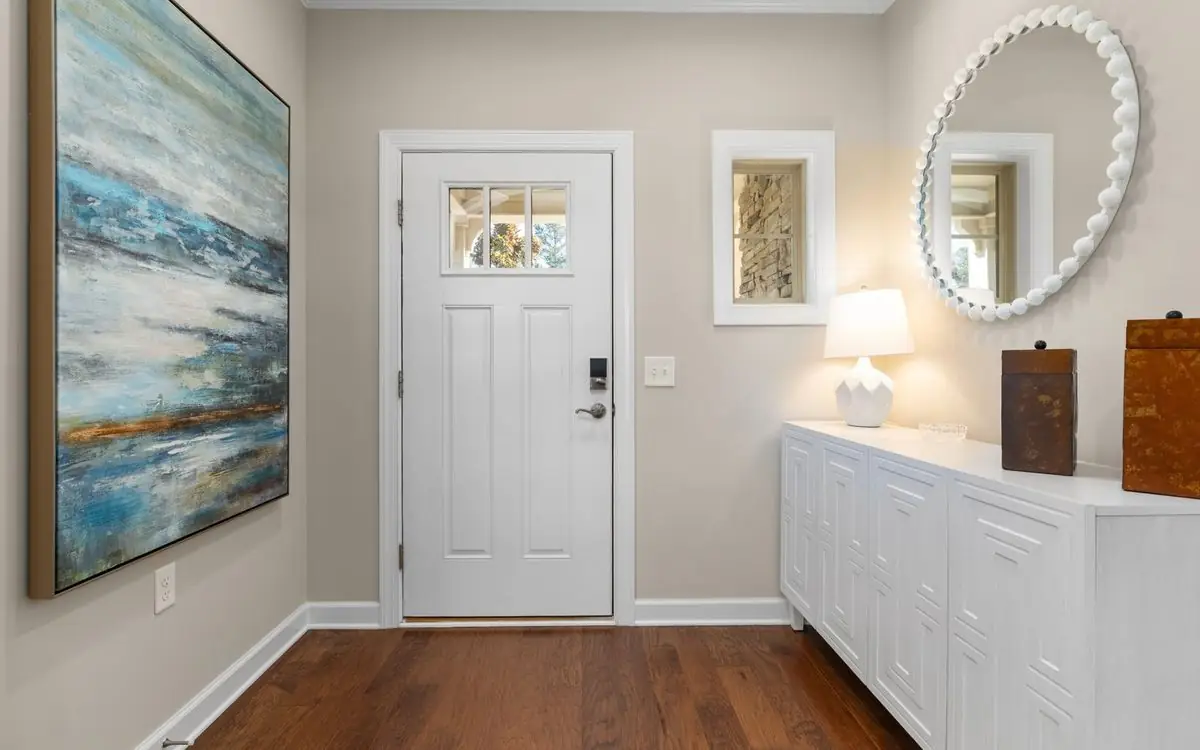 Bright entry with a white console cabinet, a round mirror, a lamp, and a clear wood floor