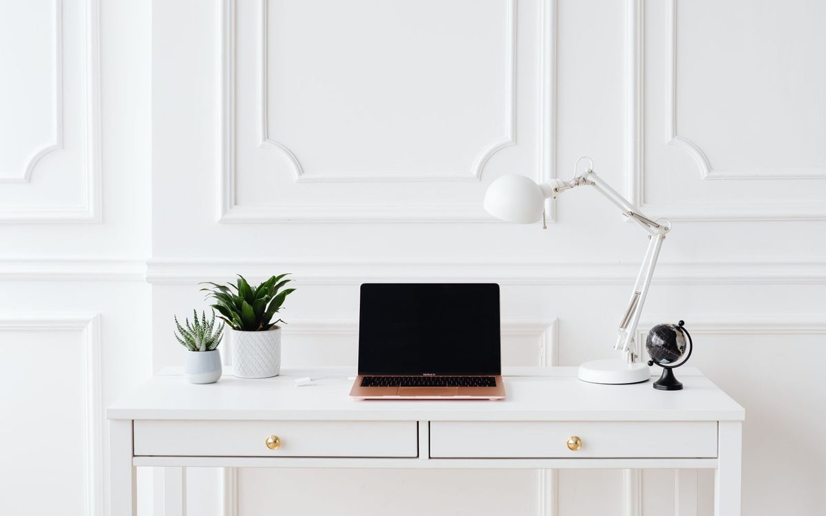 Simple home office with a clear white desk, a laptop, a lamp, and two small plants