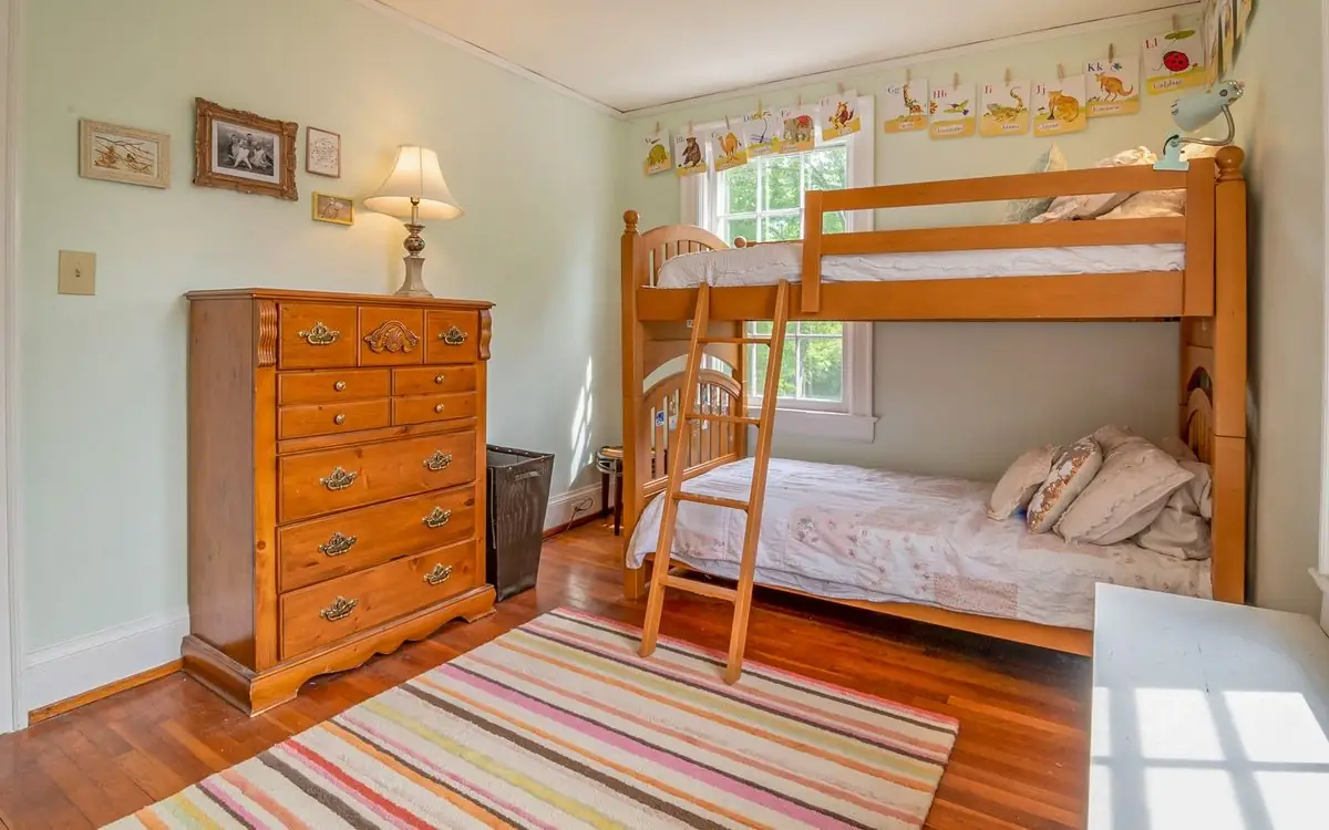Kids' bedroom with made bunk beds, a dresser, and a lamp